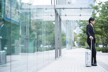 Businessman is standing in front of the building with a suitcase