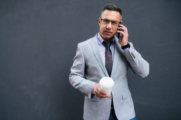 A businessman talking on his cellphone in the city while coffee break. Business on the go