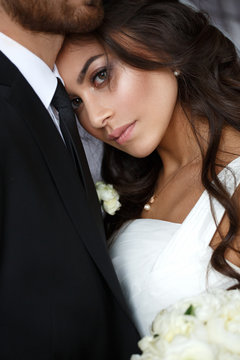 Tender wedding photo session indoor of the elegant bride in a white dress and groom in the classic tuxedo costume, family portrait