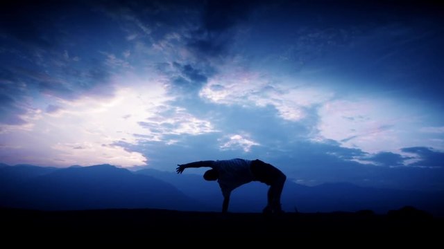 Silhouette of male acrobat doing a cartwheel on the top of a mountain. Slow motion