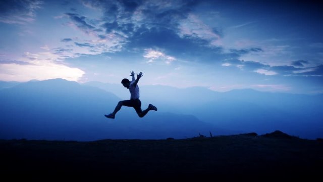 Silhouette of man jumping of happiness and success on the top of a mountain. Slow motion