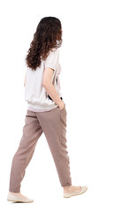 back view of walking  curly woman.  backside view of person.  Rear view people collection. Isolated over white background.Long-haired curly girl walks slowly to the side with his hands in his pockets.