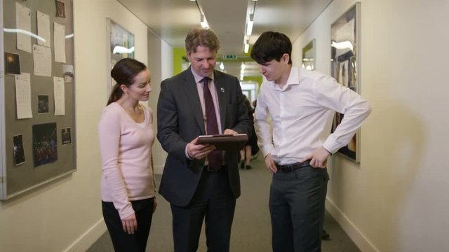  Portrait of teachers looking at computer tablet in busy school corridor