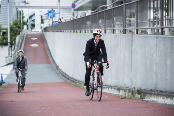 Two businessmen are commuting riding a road bike for health