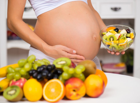 Close-up of a pregnant belly with fresh fruit and plate of salad. Healthy pregnancy, diet and vitamins
