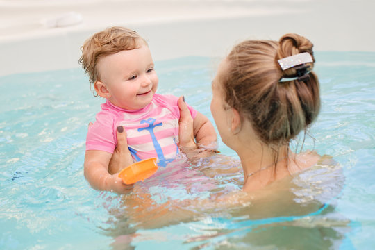 Group portrait of white Caucasian mother and baby daughter playing in water diving in swimming pool inside, looking at each other, training to swim, healthy active lifestyle