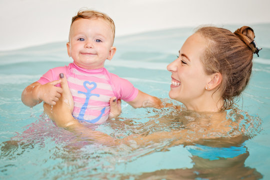 Group portrait of white Caucasian mother and baby daughter playing in water diving in swimming pool inside, looking in camera, training to swim, healthy active lifestyle