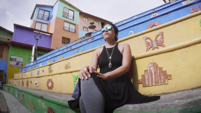 Colombian Woman seated on the stairs of the Plaza de los Zocalos, Guatape, Colombia. 4k