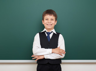 school student boy posing at the clean blackboard, grimacing and emotions, dressed in a black suit, education concept, studio photo