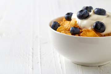 Corn flakes bowl with yogurt and blueberries on white table