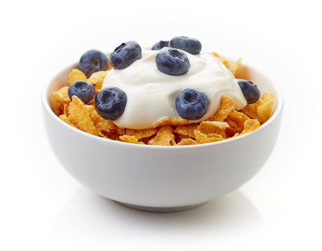 Bowl of corn flakes and blueberries with yogurt isolated on whit