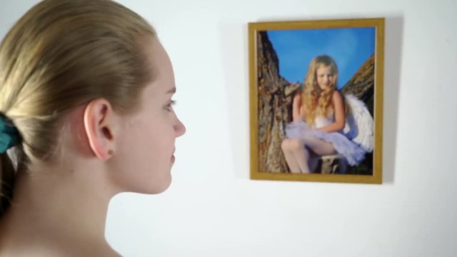 Framed photo prints hanging on the wall teenage girl holding a photograph of a little girl in frame looking at herself in the childhood
