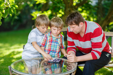 Two little kid boys and father playing together checkers game