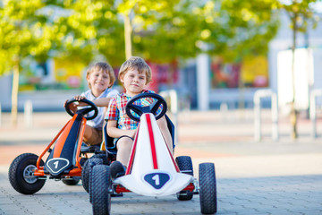 Two active little kid boys driving pedal race cars