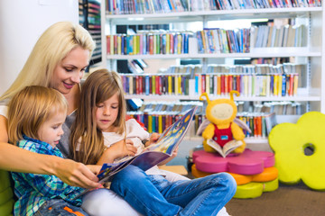 Mother with little girl and boy read book together in lounge