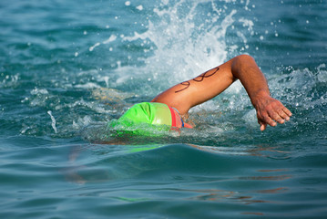 Triathlete swim in the blue sea with numbers on hand