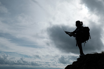 Silhouette of Girl Hikers with backpack and map on the mountain.