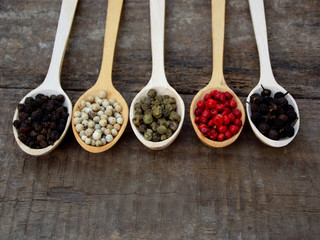 Spice. Black pepper, white, pink, green, cubeb in wooden spoons on a wooden background. Selective focus
