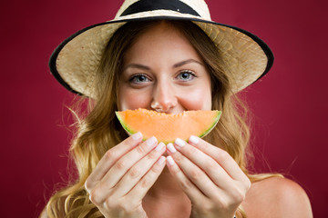 Beautiful young woman in bikini eating melon. Isolated on red.