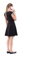 Fototapeta premium back view of a woman talking on the phone. backside view of person. Rear view people collection. Isolated over white background. Blonde in a short black dress talking on the white smartphone.
