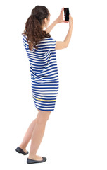 back view of standing young beautiful  woman  using a mobile phone. girl  watching. Rear view people collection.  backside view of person.  Isolated over white background. Swarthy girl in a checkered