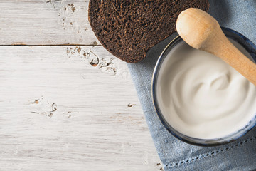 Sour cream on the ceramic dish with bread on the white wooden table top view