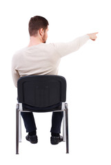 back view of young business man sitting on chair and pointing. Rear view people collection. The bearded man in a white warm sweater sits on a chair pointing sideways. 