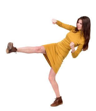 skinny woman funny fights waving his arms and legs. Isolated over white background. Long-haired brunette in a mustard-colored leg raised high.