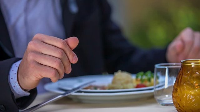 A man is in the middle of his meal. His fork and a knife are leaning on a plate and he is talking with the woman that is sitting opposite him in a restaurant. Close-up shot.
