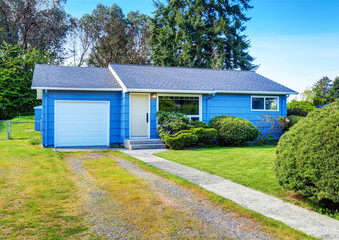 Small cute blue house with driveway and trimmed hedges.