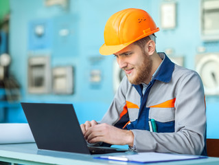 young happy engineer working at laptop in control room