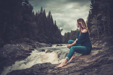 Beautiful woman posing near waterfall with mountain forest on the background.