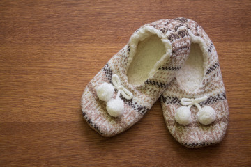 Fototapeta na wymiar Knitted slippers with pompoms on wood floor. 