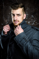 Handsome man wearing jeans clothes and a coat posing at studio. Men's beauty, seasonal fashion. Studio shot.