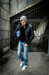 Bad boy concept. Portrait of brutal young man with short hair wearing black jacket and gray hat , Hipster style. Copy-space. Outdoor shot