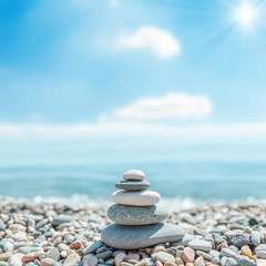 Fototapeta na wymiar stack of zen stones near sea and clouds with sun on background