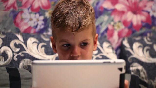 Close-up shot of little boy watching cartoon or movie on touch pad before bedtime