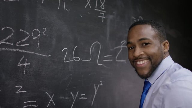  Young smiling teacher writing math formulas on blackboard