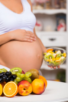 Close-up of a pregnant  tummy with fresh fruit and plate of salad. Healthy pregnancy, diet and vitamins
