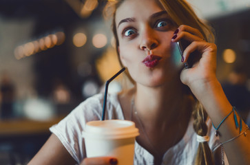 Young pretty woman using smartphone in cafe, drink coffee in cup, sweet breakfast, happy face, outdoor hipster portrait, fashion girl, table, sweet drink, tasty tea, aromatic coffee