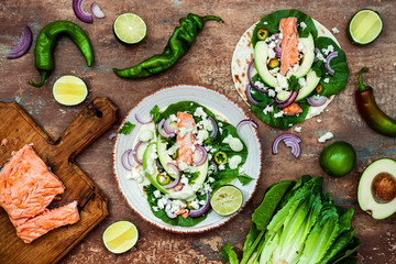 Preparing healthy lunch snacks. Fish tacos with grilled salmon, red onion, fresh salad leaves and avocado cilantro sauce on vintage stone background. Recipe for Cinco de Mayo party. Top view.