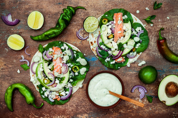 Fototapeta na wymiar Preparing healthy lunch snacks. Fish tacos with grilled salmon, red onion, fresh salad leaves and avocado cilantro sauce on vintage stone background. Recipe for Cinco de Mayo party. Top view.