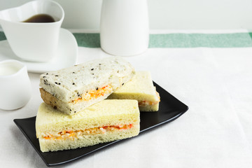 Sandwiches crab stick on the black plate with coffee and milk.