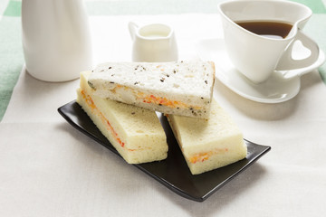 Sandwiches crab stick on the black plate with coffee and milk.