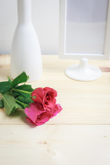 White vase, frame of photography and pink roses on the wood floor.