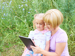 Happiness mom and daughter web surfing using tablet outdoors on