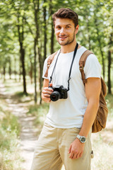 Cheerful young man photographer with modern photo camera in forest