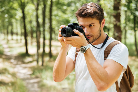 Man photographer taking pictures with modern photo camera in forest