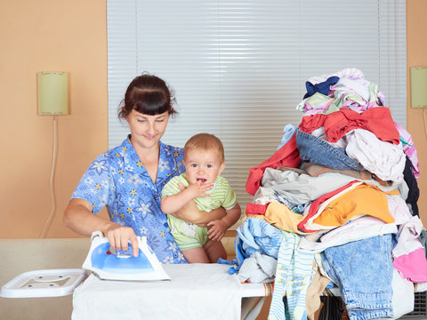 Mother holding baby in arm, ironing with the other arm.