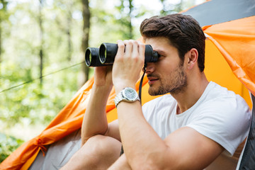 Man tourist sitting and looking at binoculars in forest